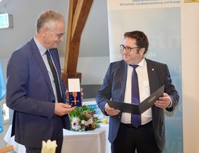 Prof. Michael Pfeifer (li) erhält das Bundesverdienstkreuz von Staatssekretär Tobias Gotthardt (Franziska Meinl/StMWI)