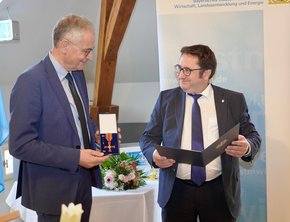 Prof. Michael Pfeifer (li) erhält das Bundesverdienstkreuz von Staatssekretär Tobias Gotthardt (Franziska Meinl/StMWI)